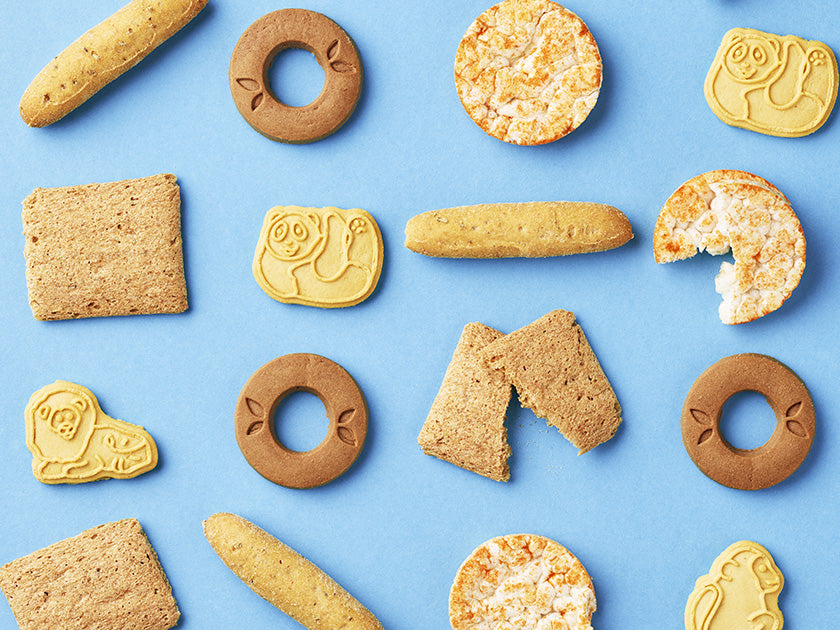 Assortiment de biscuits pour enfants aux formes variées, disposés de manière décorative sur un fond bleu. Certains biscuits sont ronds, d'autres carrés ou en forme d'animaux.