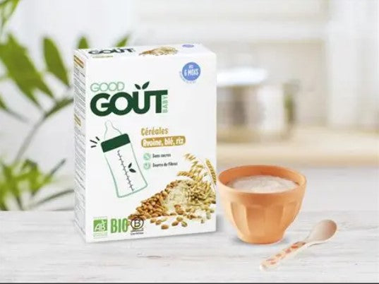 Boîte de céréales bio pour bébé de la marque "Good Goût", saveur avoine, blé et riz, posée sur un plan de travail. À côté, un bol de céréales prêtes à consommer avec une petite cuillère.