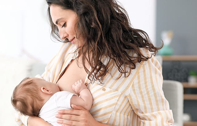 Maman souriante allaite son bébé dans un environnement lumineux et chaleureux.